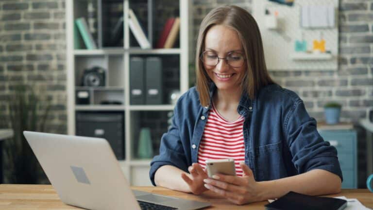 Woman using a smartphone while sitting in front of a laptop