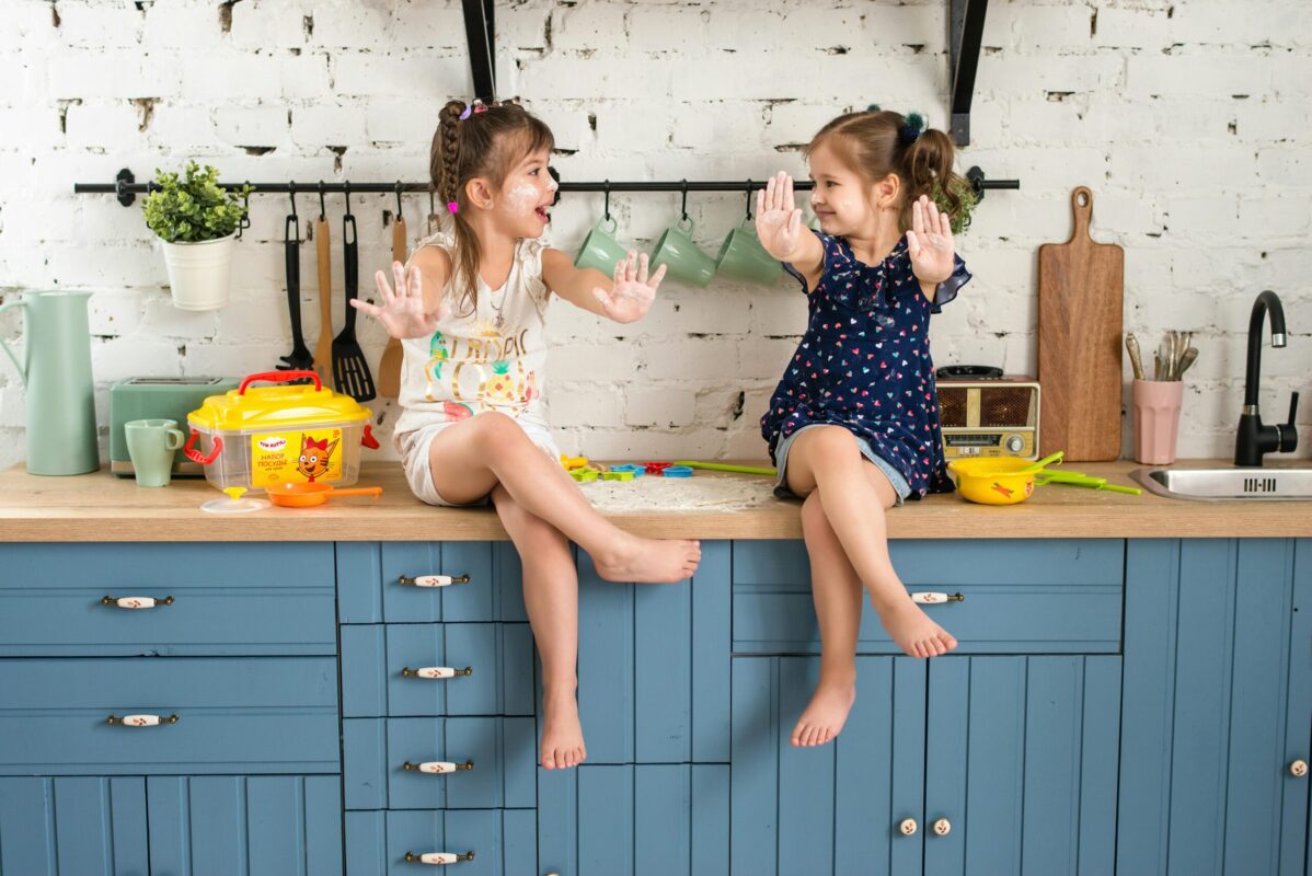 Fun spring activities for kids at home – two young girls enjoying messy play in the kitchen with flour, laughter, and creative screen-free fun.